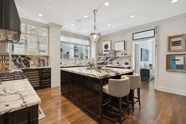 kitchen featuring glass insert cabinets, a center island, light stone countertops, extractor fan, and pendant lighting