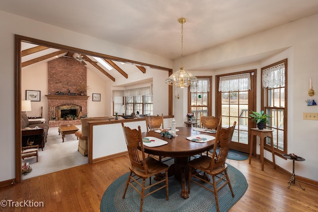 dining area with lofted ceiling with beams, ceiling fan with notable chandelier, a fireplace, and light hardwood / wood-style flooring