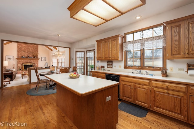 kitchen with a kitchen island, decorative light fixtures, dishwasher, sink, and light wood-type flooring