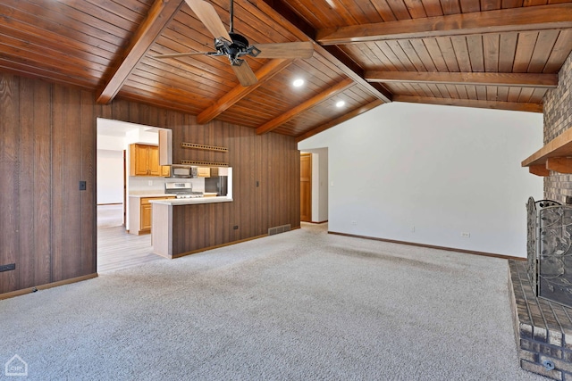 unfurnished living room featuring ceiling fan, wooden walls, a fireplace, lofted ceiling with beams, and light colored carpet