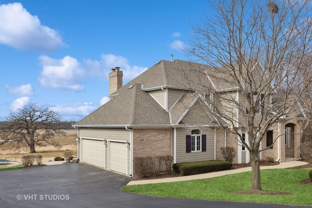 view of side of home with driveway, a garage, a shingled roof, a chimney, and brick siding