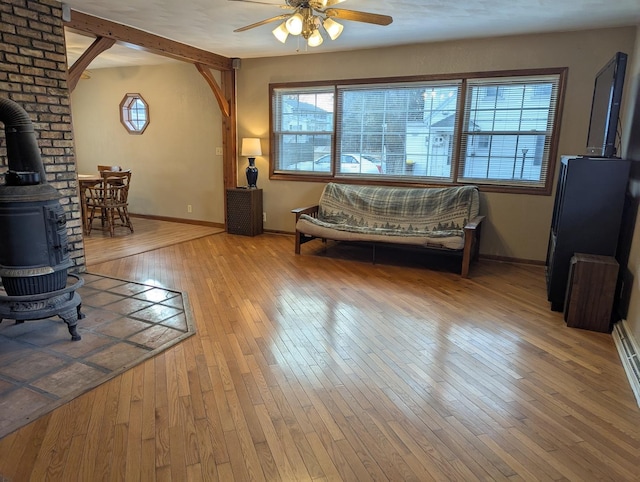 living room featuring wood-type flooring, a wood stove, a wealth of natural light, and ceiling fan