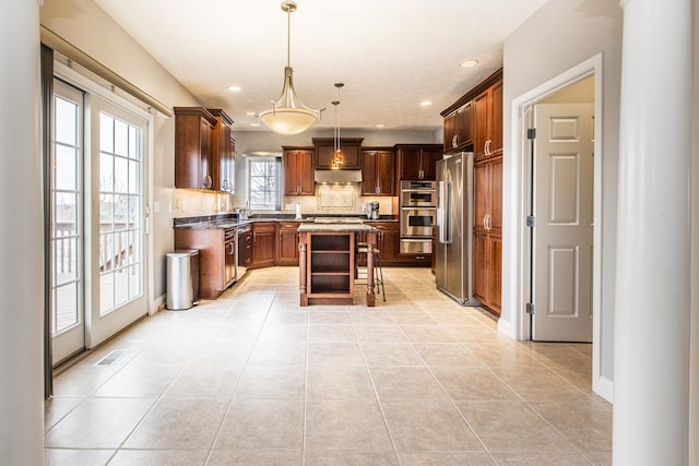 kitchen with a kitchen island, a kitchen bar, hanging light fixtures, light tile patterned floors, and stainless steel appliances