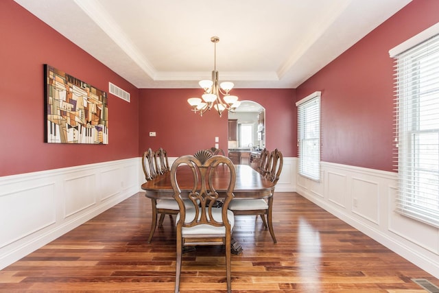 dining area with dark wood-type flooring, crown molding, a raised ceiling, and an inviting chandelier