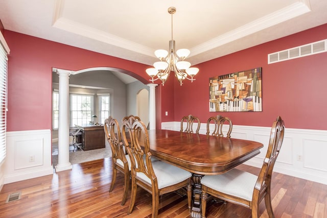 dining room with a raised ceiling, hardwood / wood-style floors, and decorative columns