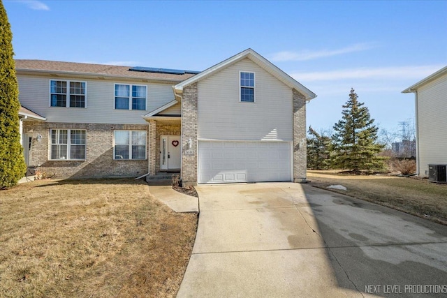 traditional-style home featuring brick siding, solar panels, concrete driveway, an attached garage, and a front yard