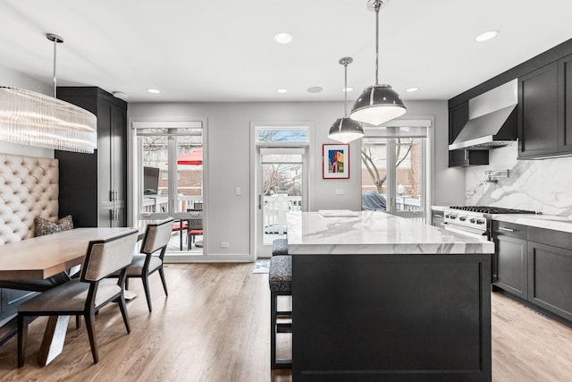 kitchen featuring light stone counters, a center island, wall chimney range hood, and light wood finished floors