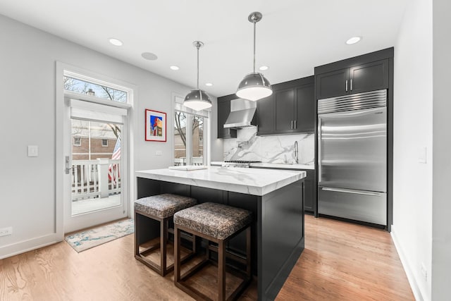 kitchen with wall chimney exhaust hood, appliances with stainless steel finishes, light wood-style flooring, and decorative backsplash