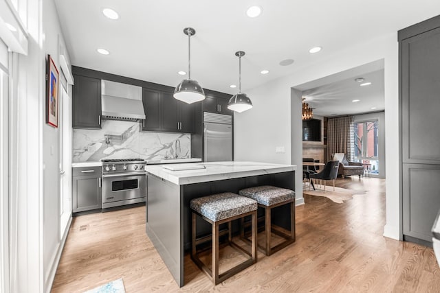 kitchen featuring light wood finished floors, high end appliances, a kitchen island, light stone countertops, and wall chimney range hood