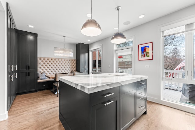 kitchen featuring dark cabinetry, plenty of natural light, light wood finished floors, and light stone countertops