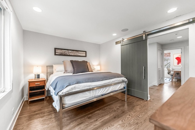 bedroom with a barn door, baseboards, wood finished floors, and recessed lighting