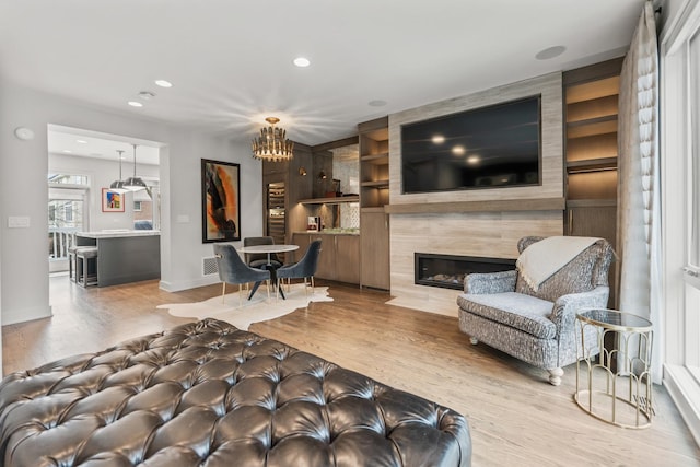 living room featuring built in shelves, a fireplace, visible vents, wood finished floors, and baseboards