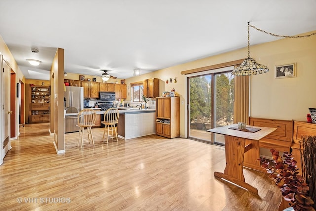 kitchen featuring brown cabinets, freestanding refrigerator, a peninsula, light wood-type flooring, and black microwave