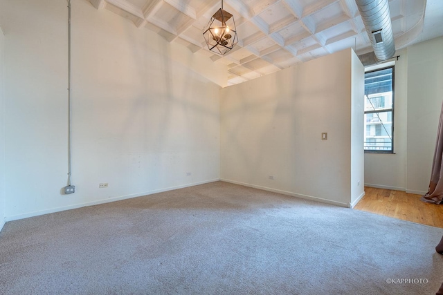 carpeted empty room featuring a chandelier and beam ceiling