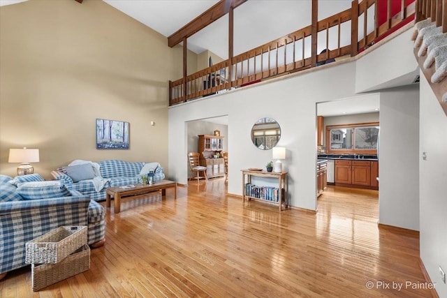 living area featuring beam ceiling, a towering ceiling, and light wood finished floors