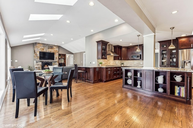 dining space with vaulted ceiling with skylight, a stone fireplace, recessed lighting, and light wood-style floors