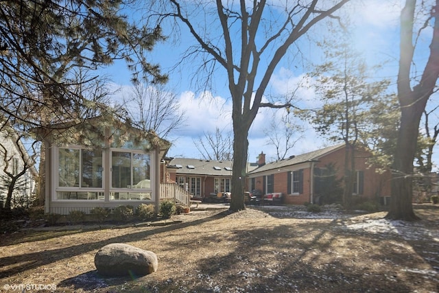 view of side of property featuring a sunroom, a chimney, and brick siding