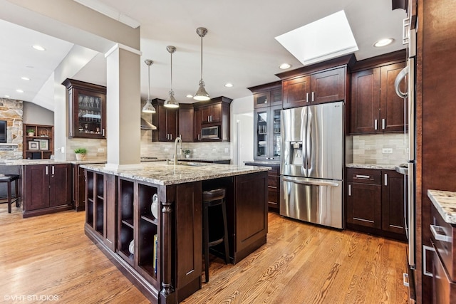 kitchen with a skylight, glass insert cabinets, a breakfast bar, stainless steel appliances, and a sink