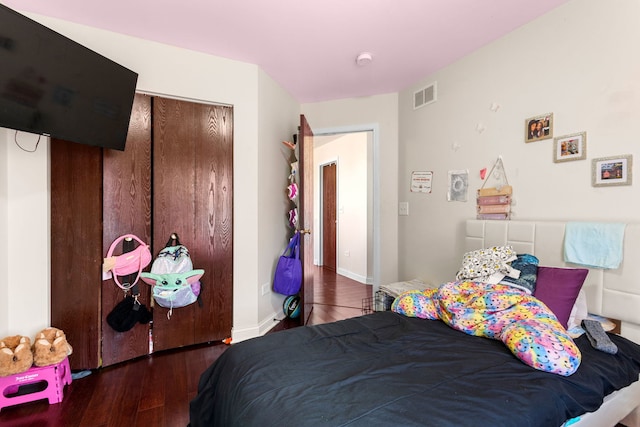 bedroom with a closet, wood finished floors, visible vents, and baseboards