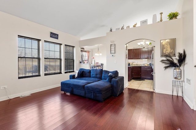 living area with light wood-type flooring, vaulted ceiling, a notable chandelier, and baseboards