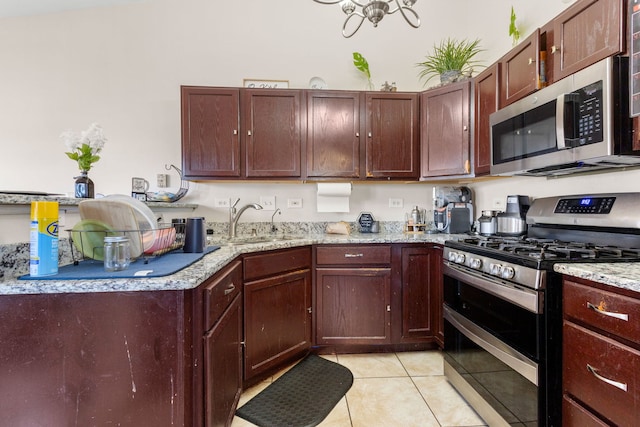 kitchen with appliances with stainless steel finishes, light tile patterned flooring, a sink, and light stone counters