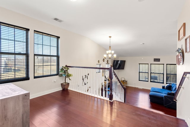 unfurnished room with lofted ceiling, visible vents, an inviting chandelier, wood finished floors, and baseboards