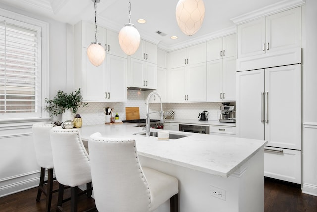 kitchen with pendant lighting, sink, white cabinetry, a kitchen breakfast bar, and paneled fridge