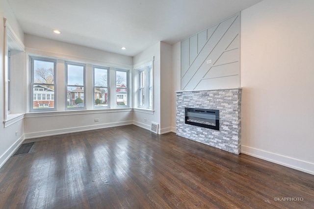 unfurnished living room with dark hardwood / wood-style floors, a stone fireplace, and a wealth of natural light