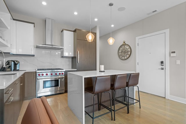 kitchen featuring hanging light fixtures, a center island, white cabinets, designer stove, and wall chimney exhaust hood