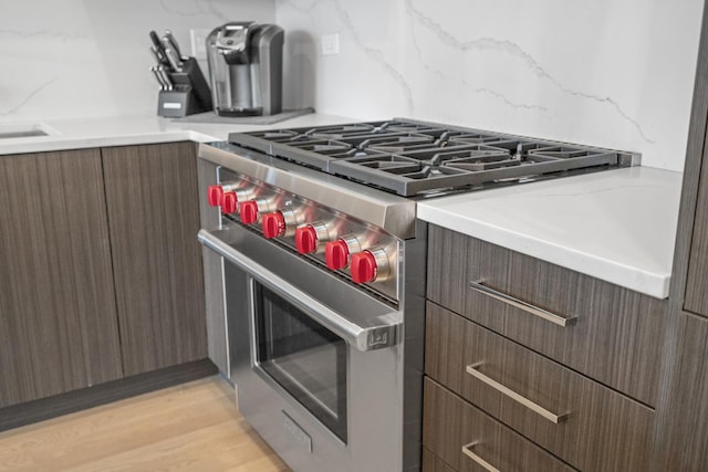 kitchen with tasteful backsplash, high end stainless steel range, and light hardwood / wood-style flooring