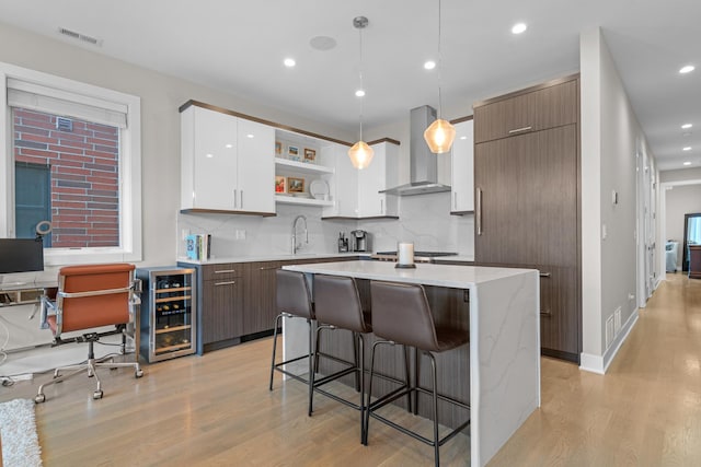 kitchen featuring a kitchen island, pendant lighting, white cabinetry, beverage cooler, and wall chimney exhaust hood