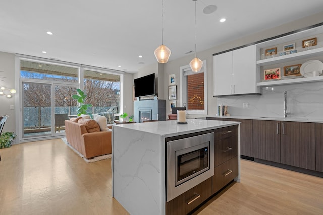 kitchen featuring dark brown cabinetry, white cabinetry, light stone counters, stainless steel microwave, and pendant lighting