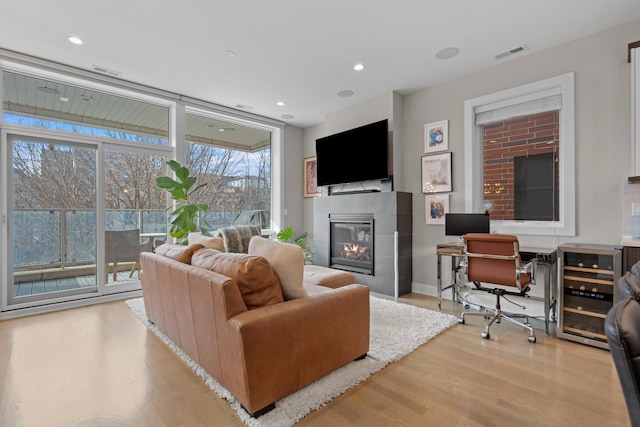 living room featuring a wall of windows, a tile fireplace, light hardwood / wood-style floors, and beverage cooler