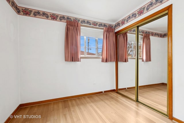 unfurnished bedroom featuring ornamental molding, a closet, baseboards, and wood finished floors