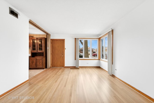 empty room with visible vents, light wood-style flooring, and baseboards