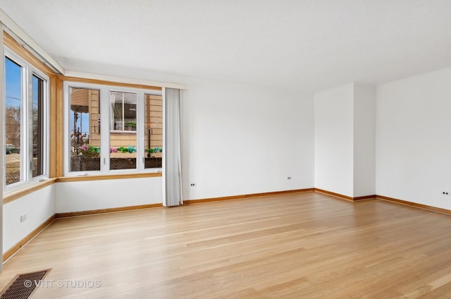 empty room with light wood-style flooring, visible vents, and baseboards