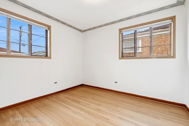 spare room with ornamental molding, baseboards, and light wood finished floors