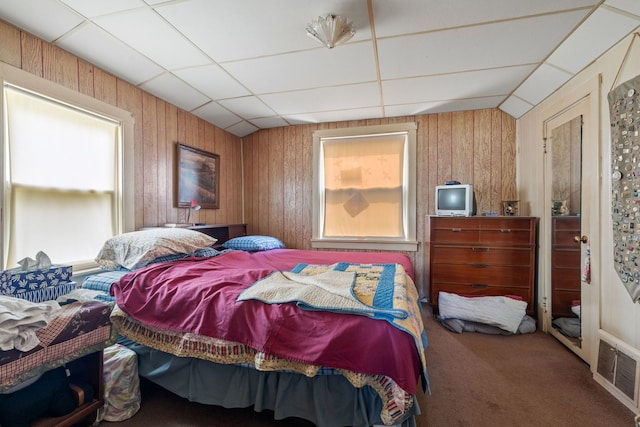 bedroom featuring a drop ceiling, carpet, and wood walls