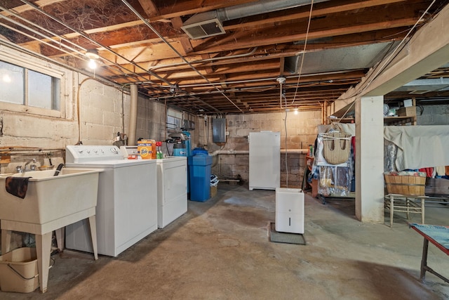 basement featuring white refrigerator, electric panel, and separate washer and dryer