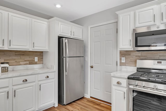 kitchen featuring light stone countertops, appliances with stainless steel finishes, white cabinets, and decorative backsplash