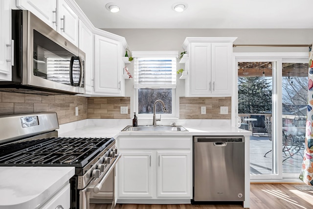 kitchen featuring sink, white cabinetry, backsplash, stainless steel appliances, and light wood-type flooring