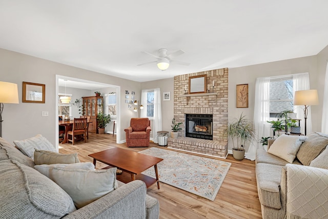 living room with ceiling fan, a brick fireplace, and light hardwood / wood-style floors