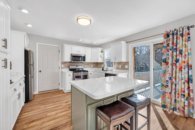 kitchen with sink, a breakfast bar area, white cabinetry, appliances with stainless steel finishes, and decorative backsplash