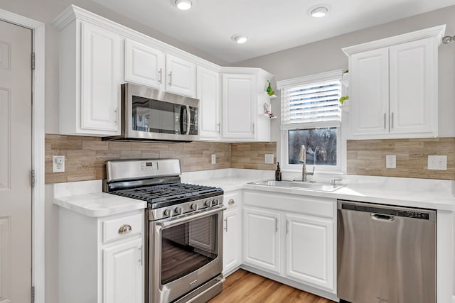 kitchen with sink, light hardwood / wood-style flooring, appliances with stainless steel finishes, decorative backsplash, and white cabinets