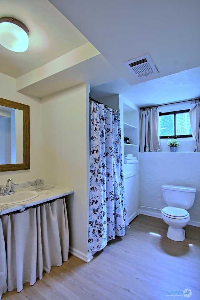 bathroom with visible vents, wood finished floors, toilet, baseboards, and a sink