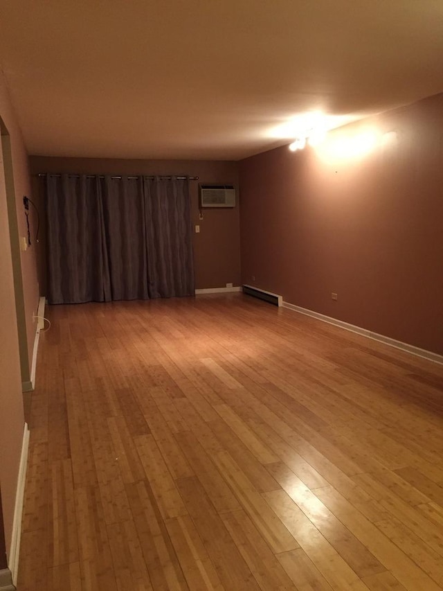 unfurnished room with a wall mounted air conditioner, light hardwood / wood-style floors, and baseboard heating