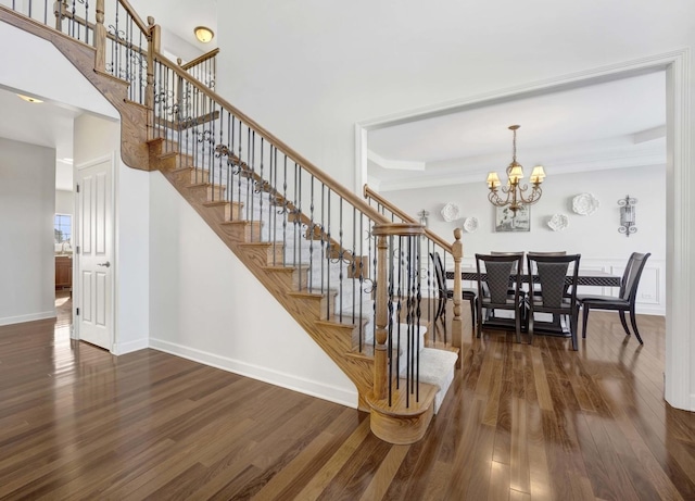 stairway featuring an inviting chandelier, wood finished floors, and baseboards