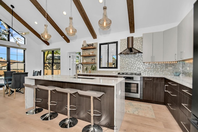 kitchen with appliances with stainless steel finishes, sink, decorative light fixtures, wall chimney exhaust hood, and a kitchen island with sink