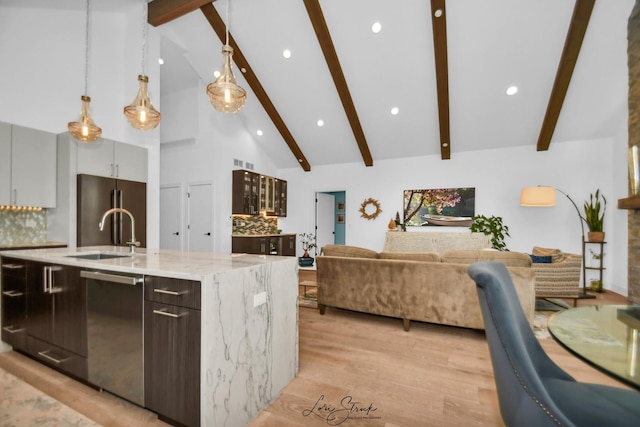 kitchen featuring a center island with sink, stainless steel appliances, decorative light fixtures, sink, and light stone counters