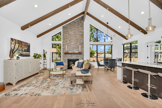 living room featuring high vaulted ceiling, beamed ceiling, a stone fireplace, and light hardwood / wood-style flooring